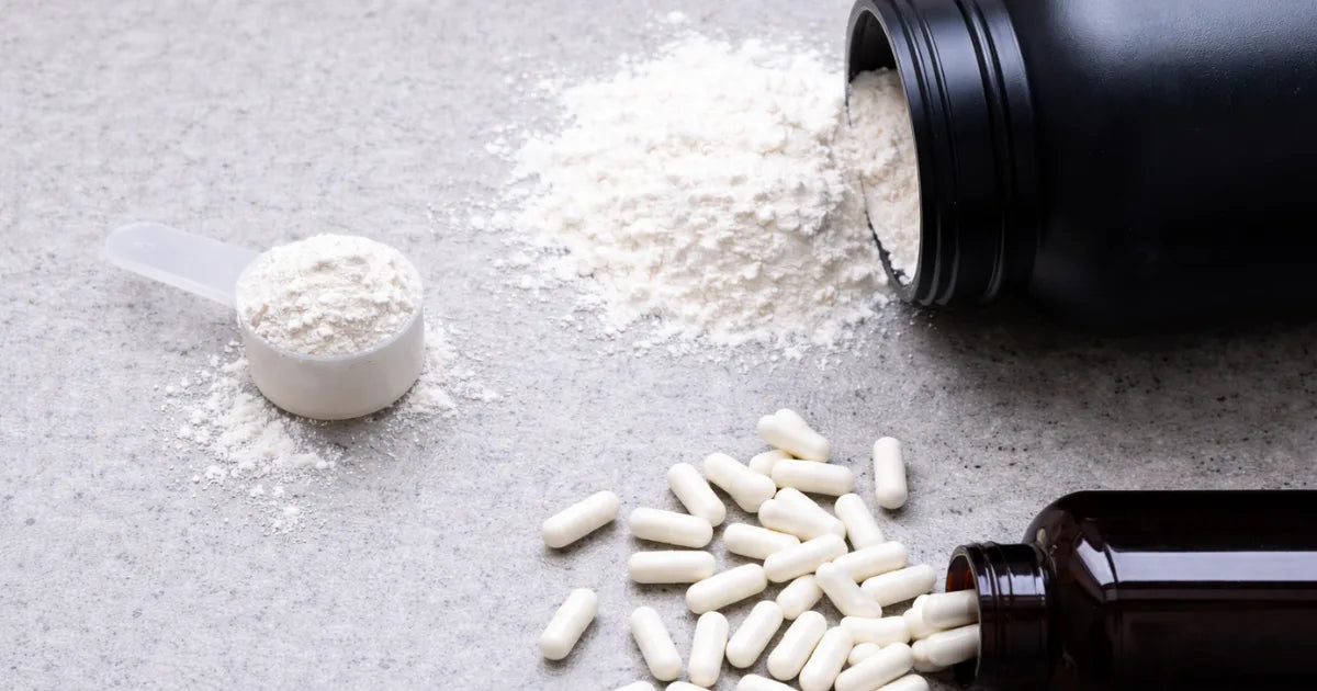 Spilled white creatine powder with a scoop and capsules from supplement bottles
